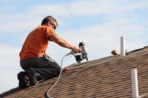 Person inspecting roof shingles and gutters from the ground after a storm, with branches and debris nearby.